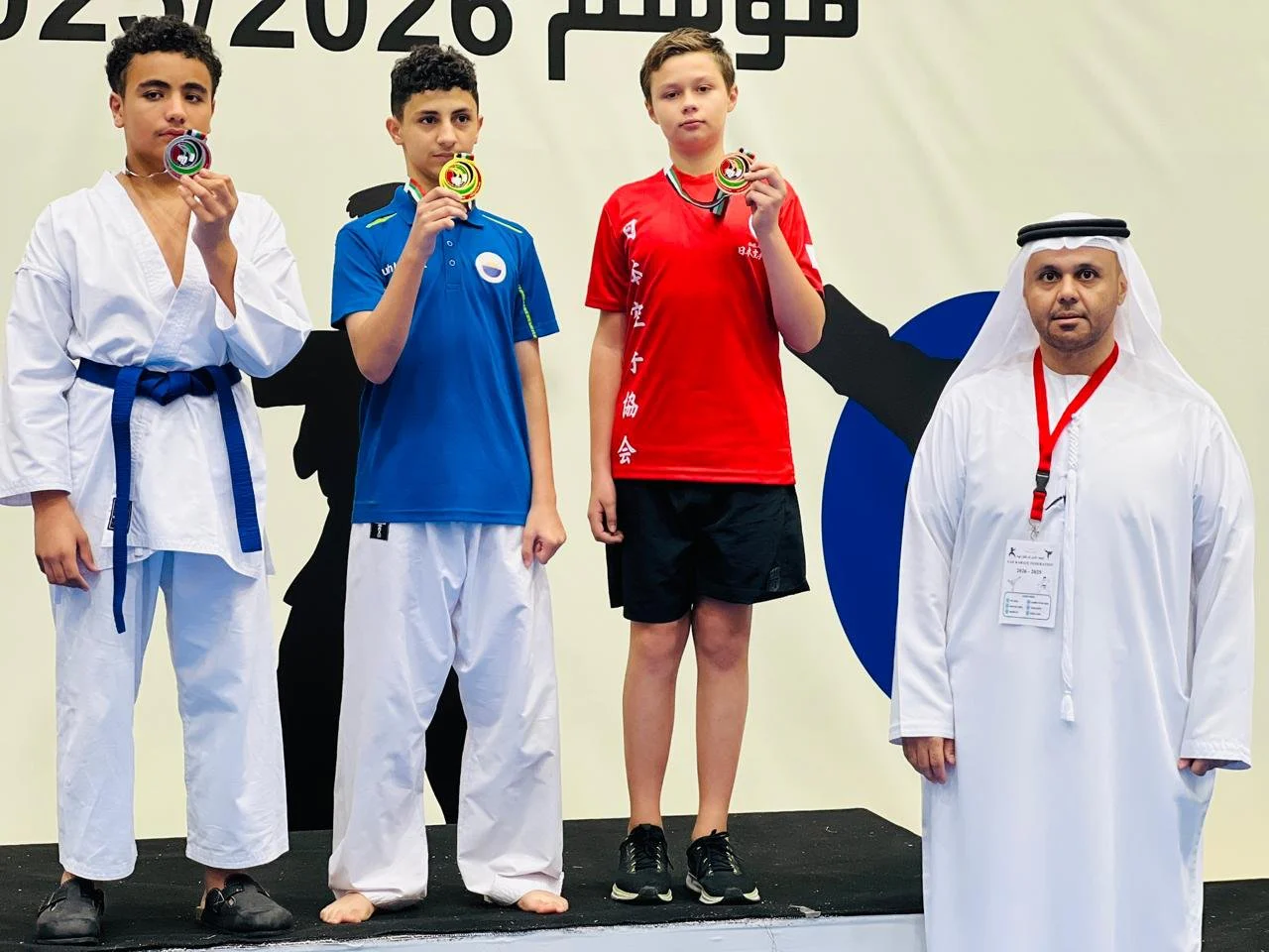 Three teenage medallists on the podium biting their medals at a karate competition