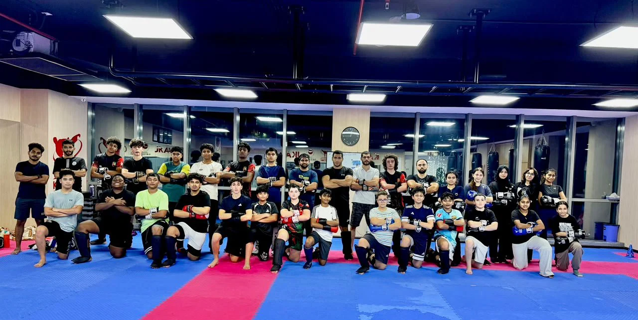 Large group of teenage and adult kickboxing students posing with arms crossed in the gym