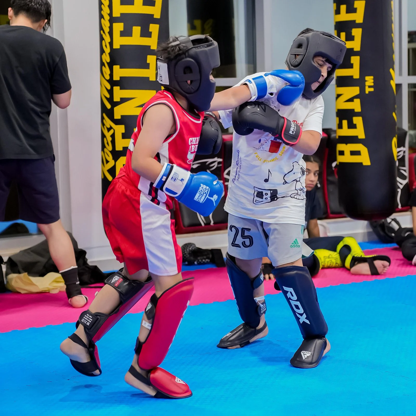 Two young kickboxers in head guards, gloves and shin guards sparring on the mats