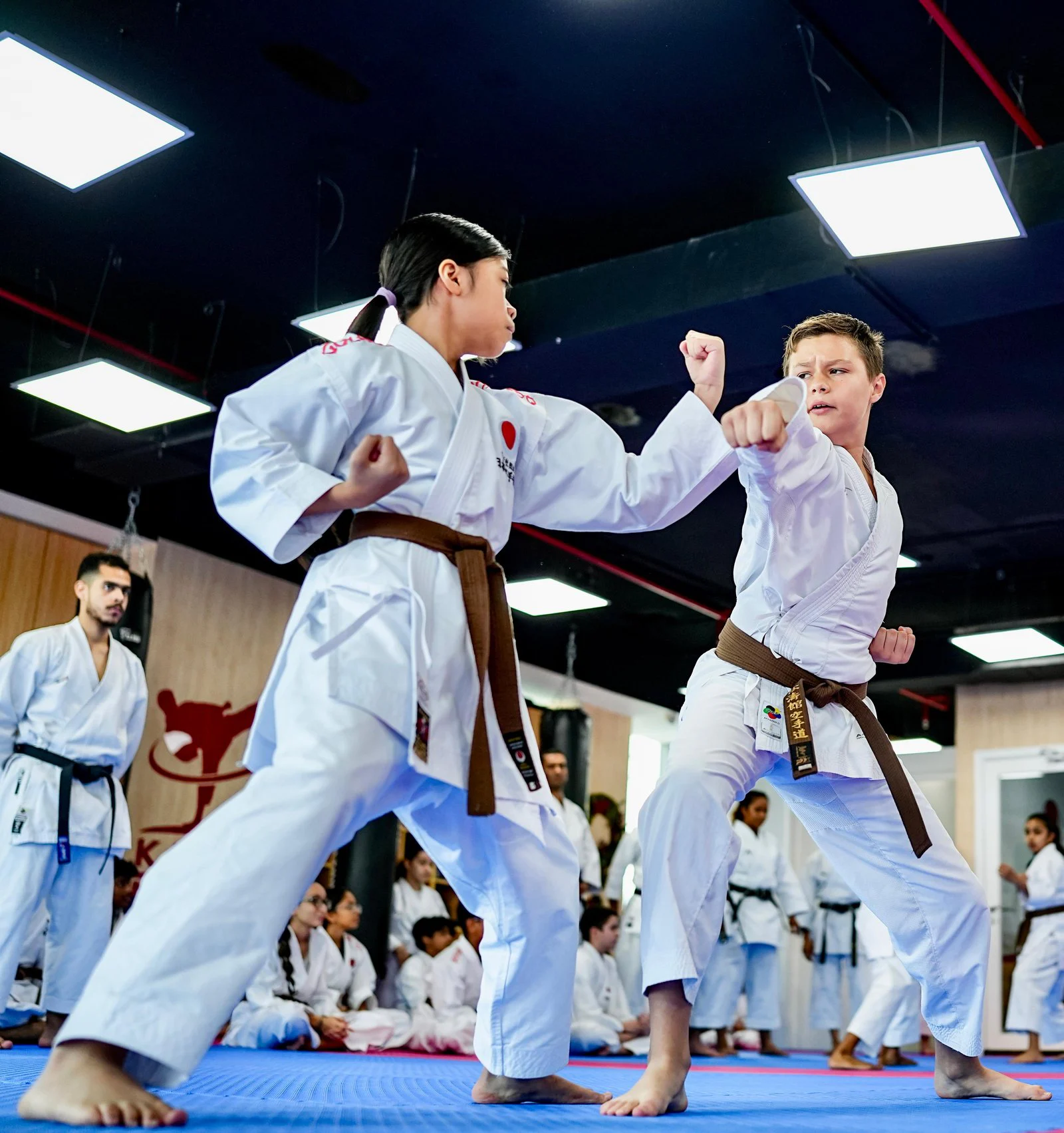 Two brown belt students practising a punch and block drill while an instructor watches