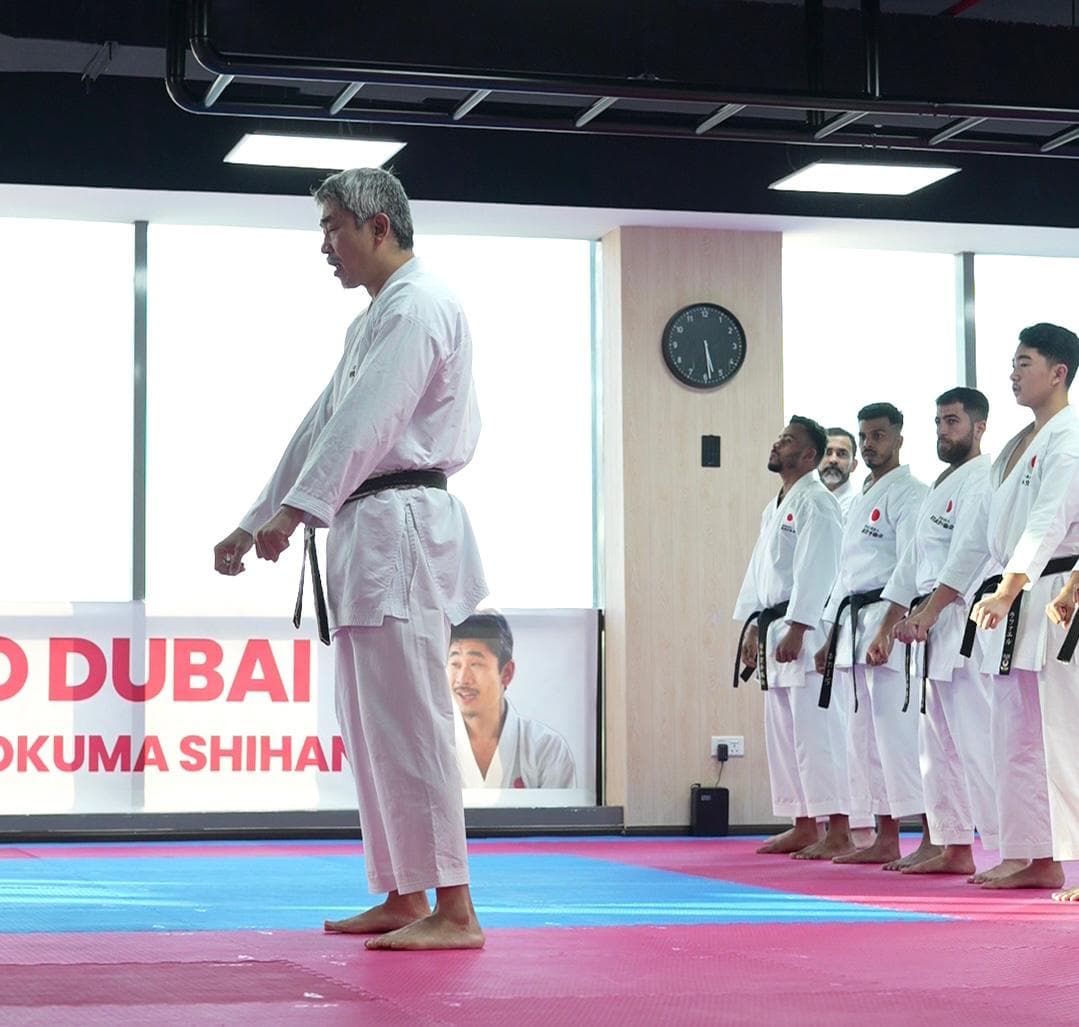Senior JKA instructor in white gi standing before a line of black belt students on pink and blue mats