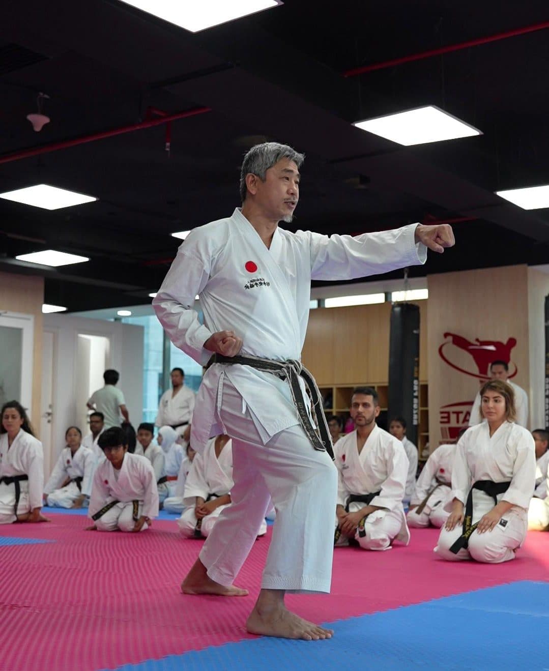 Instructor demonstrating a straight punch while seated students watch from the mats