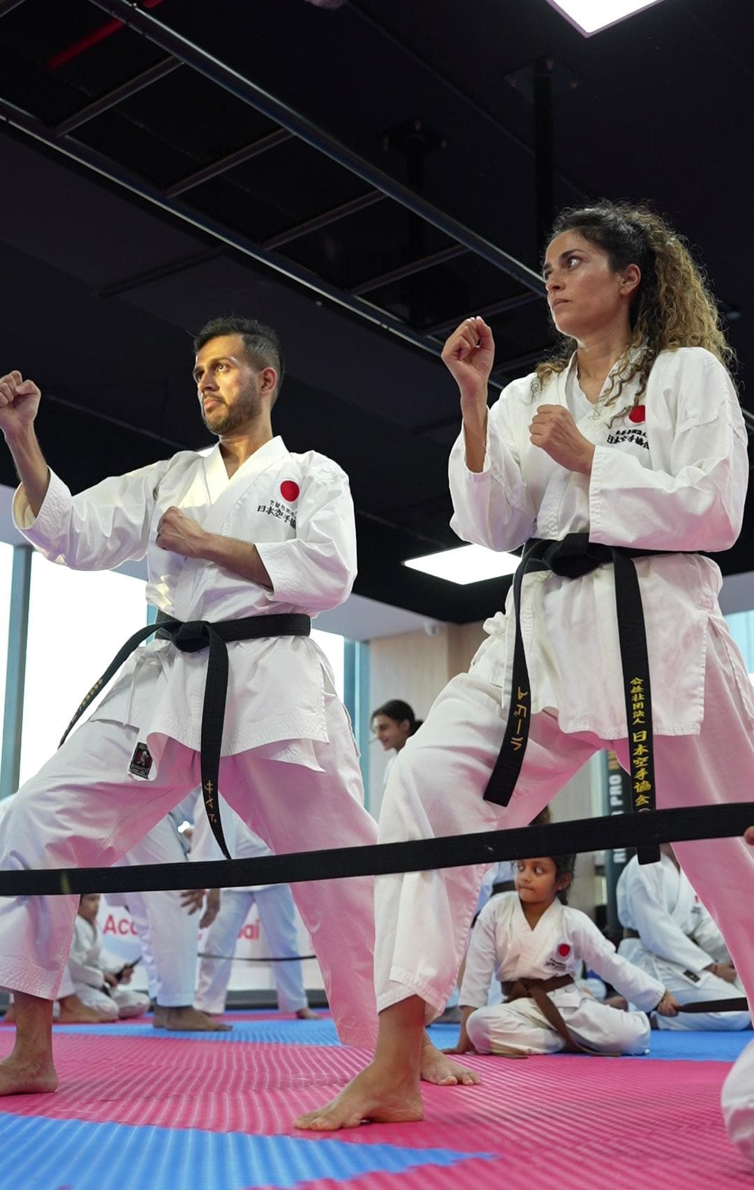 Two black belt students, a man and a woman, holding a guard position side by side during adult karate practice