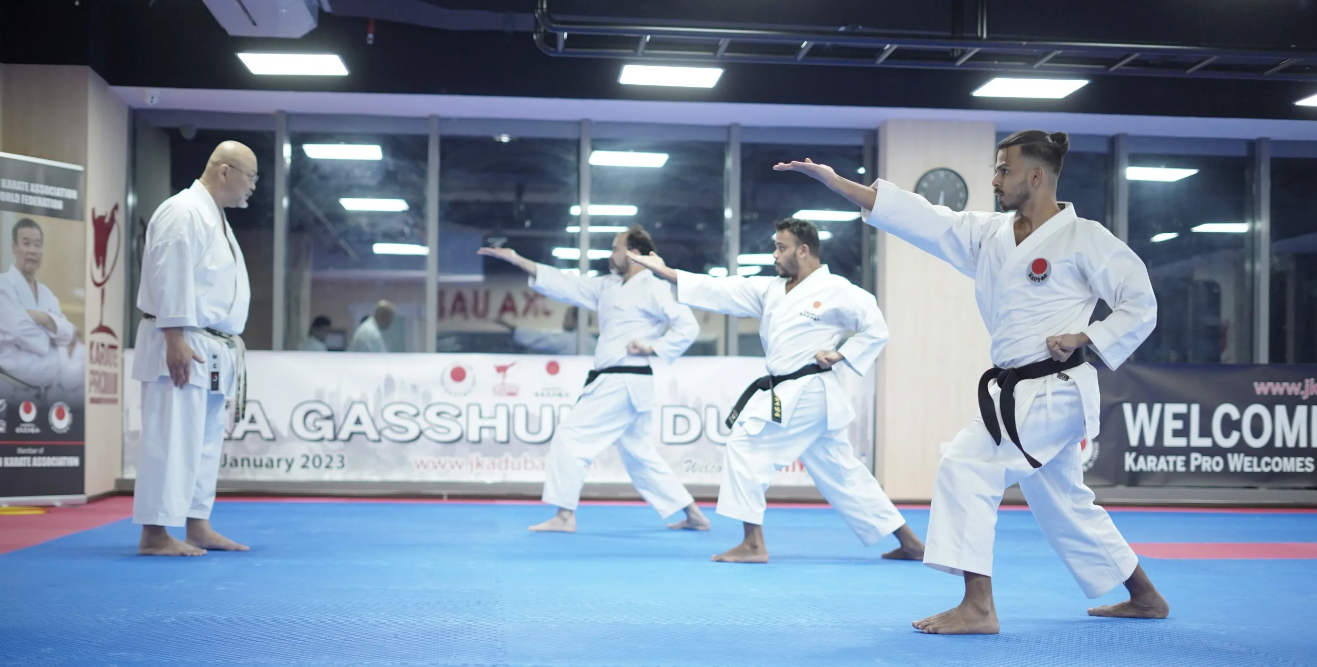 Karateka executing a front kick during a JKA Gasshuku Dubai seminar with instructors watching in the background