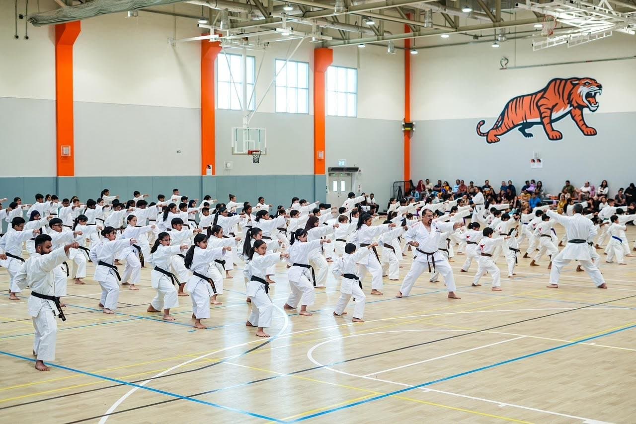 Karatekas practising kata in rows at a JKA Gasshuku seminar as spectators watch from the bleachers