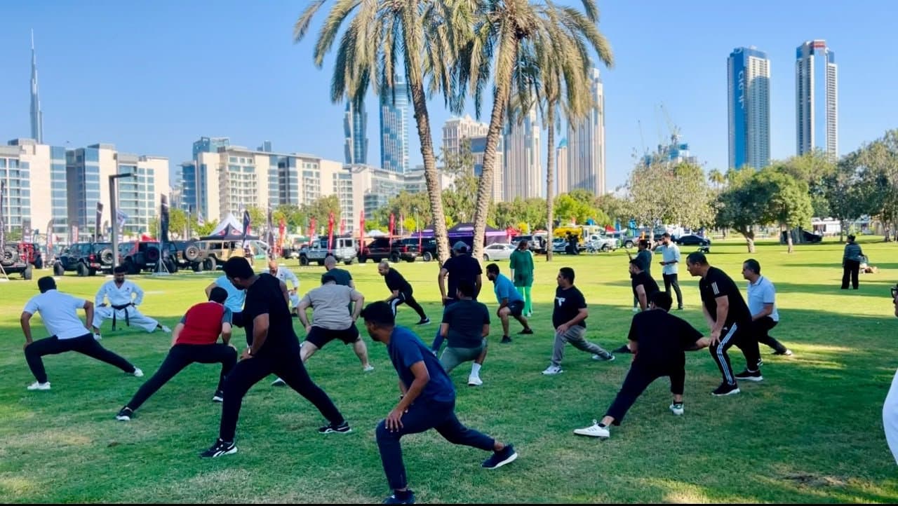 Students stretching and practising lunges together on the grass with the Downtown Dubai skyline in the background