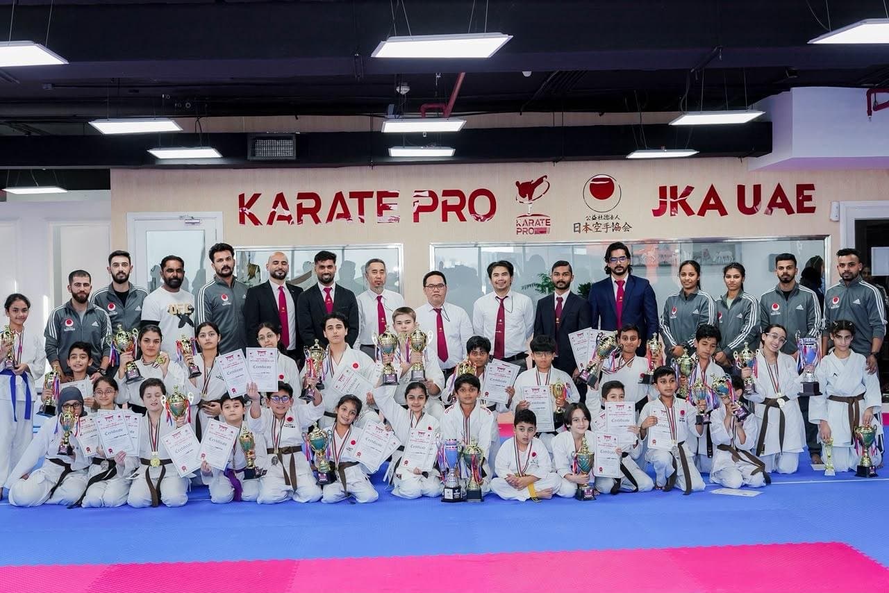 Karate Pro instructors in suits and red ties standing behind students holding trophies, medals and certificates at an awards day