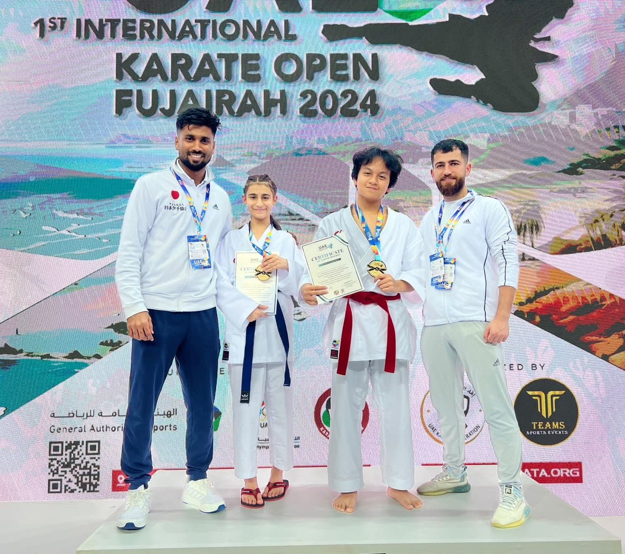 Two young medallists posing with their coaches at the 1st International Karate Open Fujairah 2024