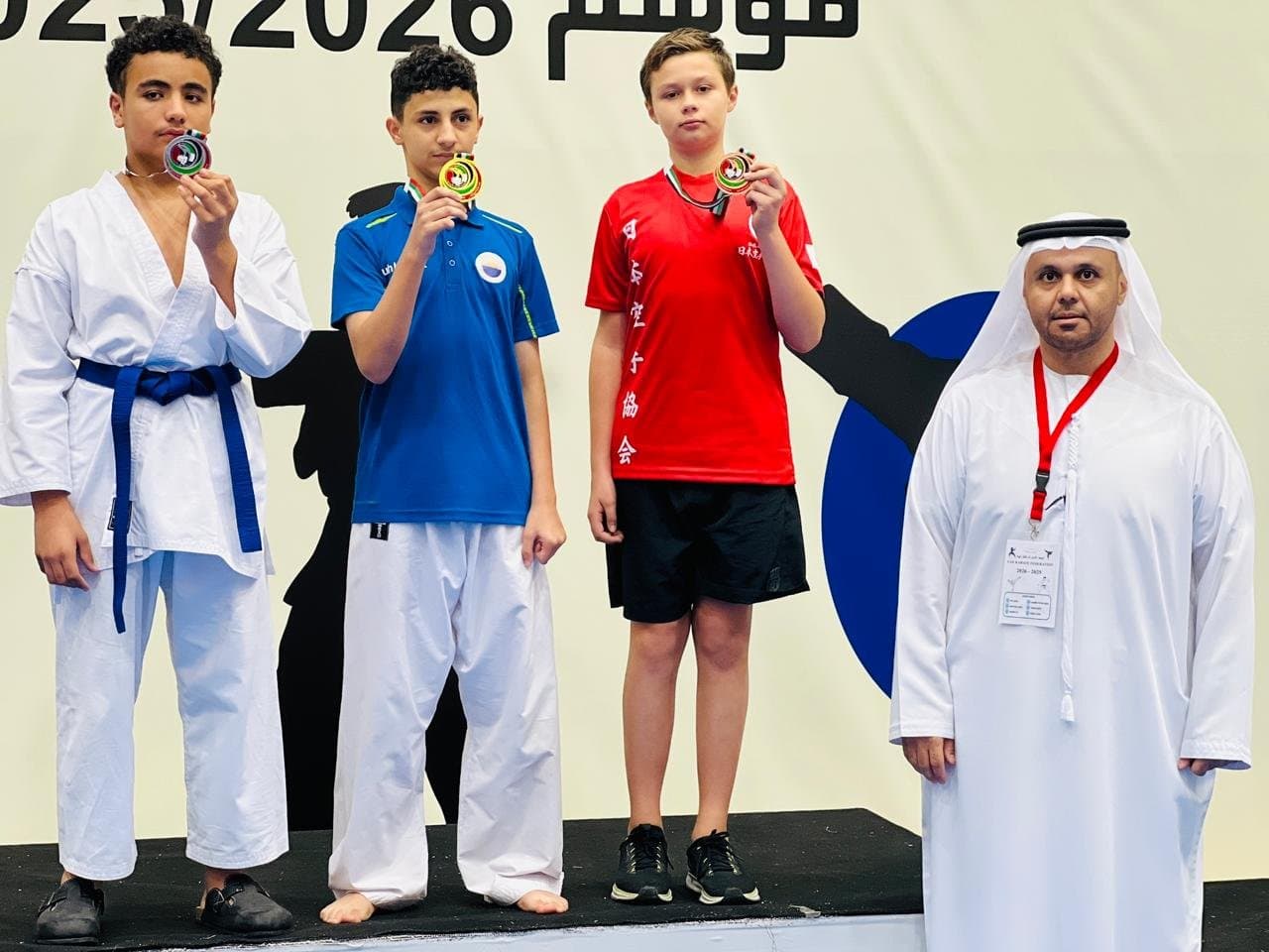 Three teenage medallists on the podium biting their medals at a karate competition