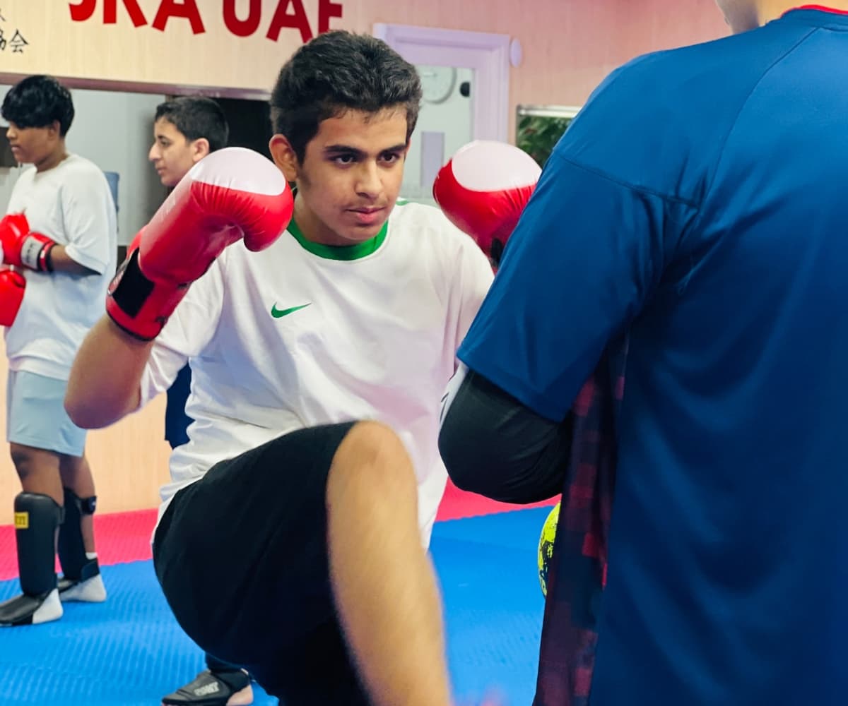 Teenage kickboxer in red gloves squaring up to a coach holding a focus mitt