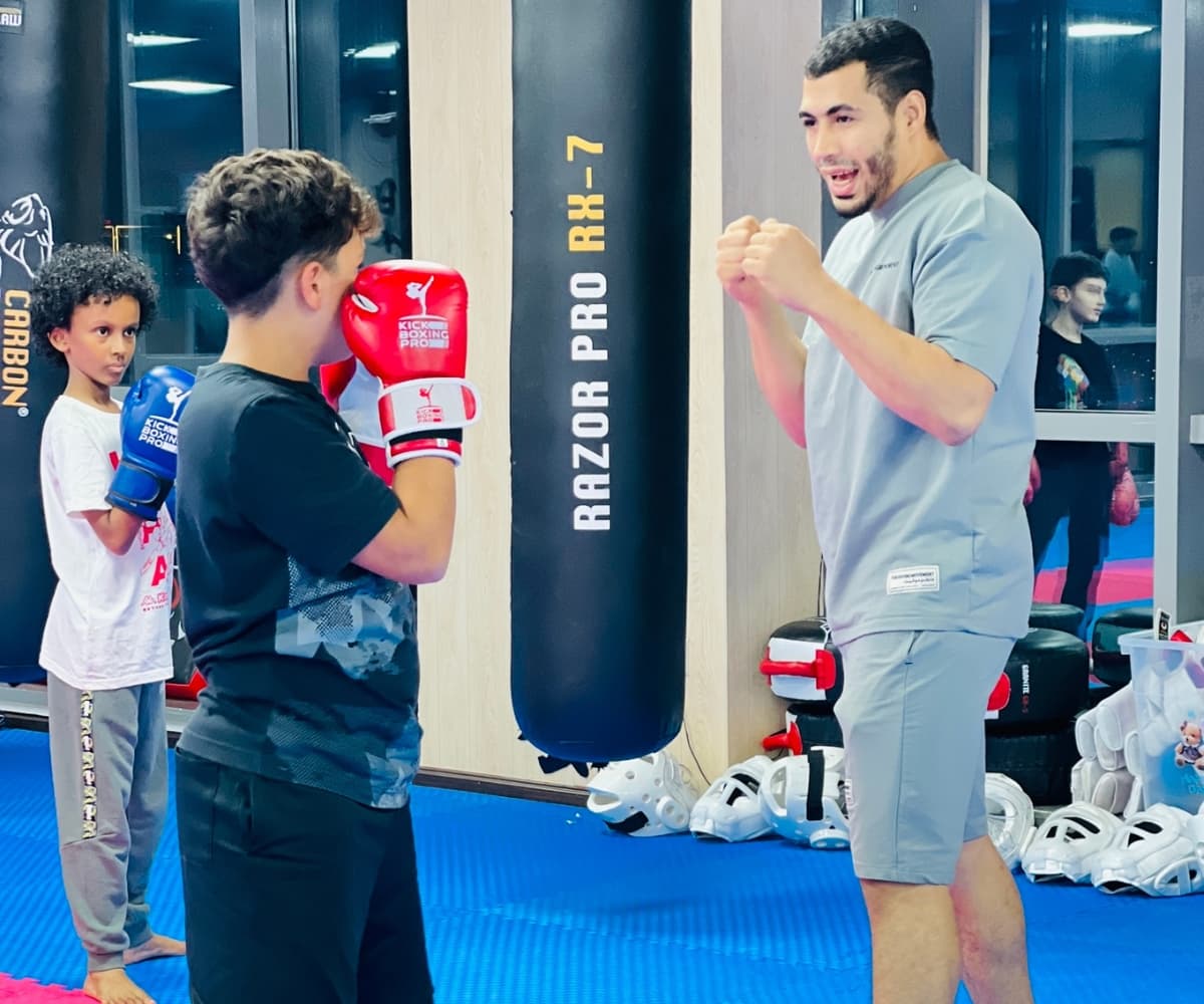 Coach guiding a young student's guard beside the Razor Pro heavy bags in the dojo