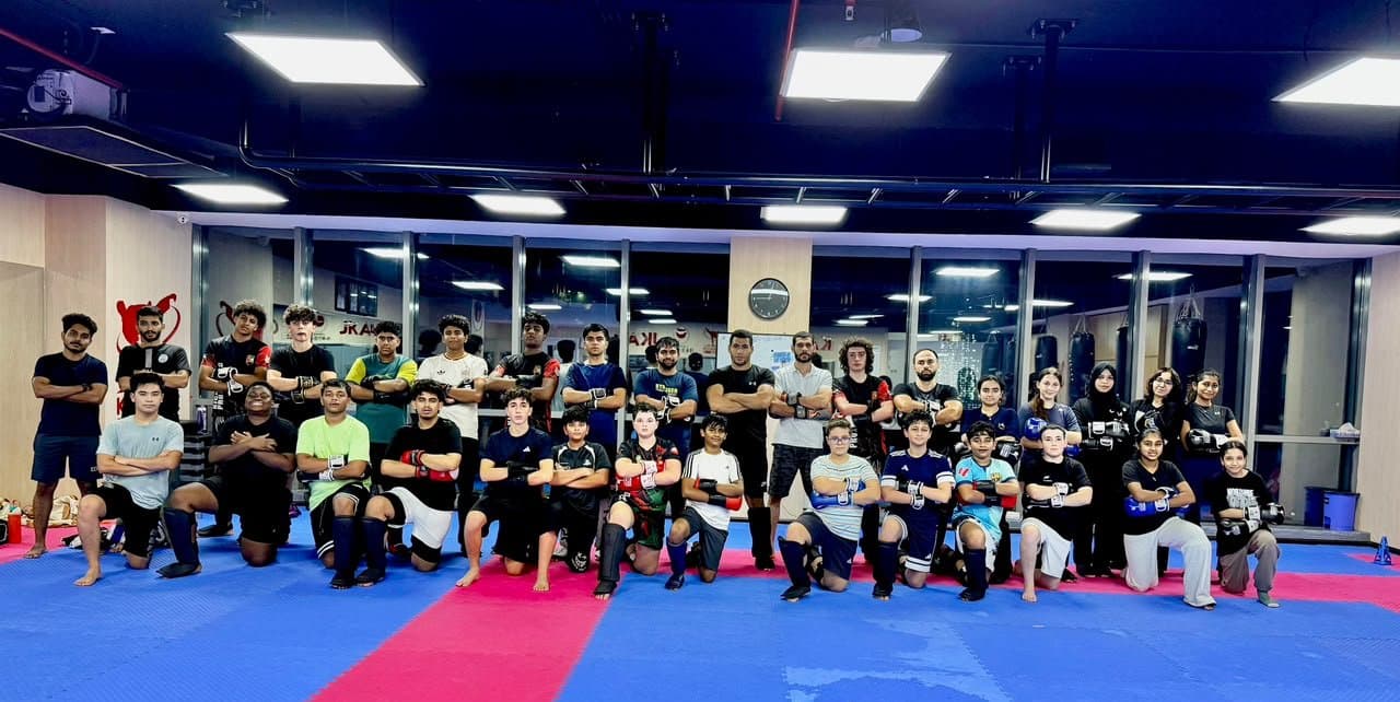Second group photo of teenage and adult kickboxing students posing with arms crossed in the gym
