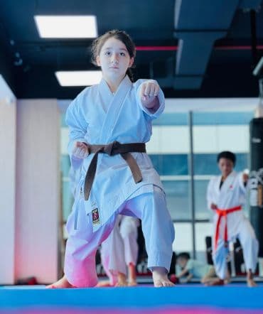 Young girl in brown belt holding a punching stance on blue mats in the dojo