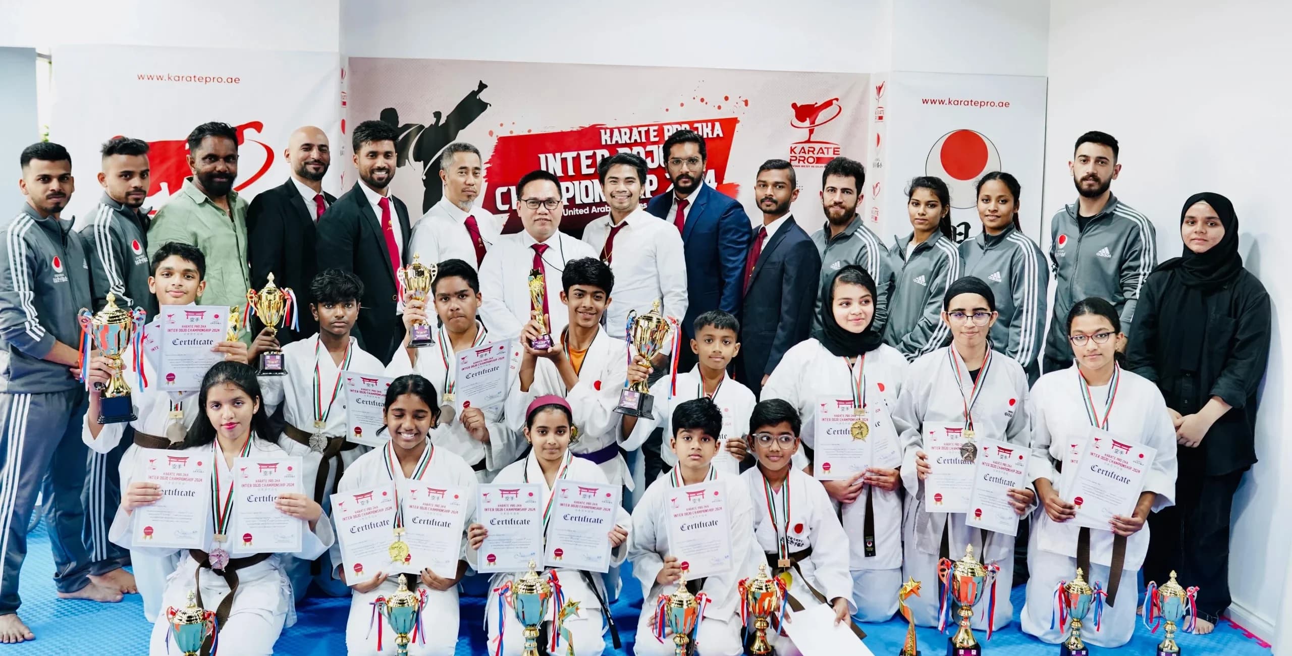 Large group of kids with trophies, medals and certificates posing with instructors and parents in the dojo
