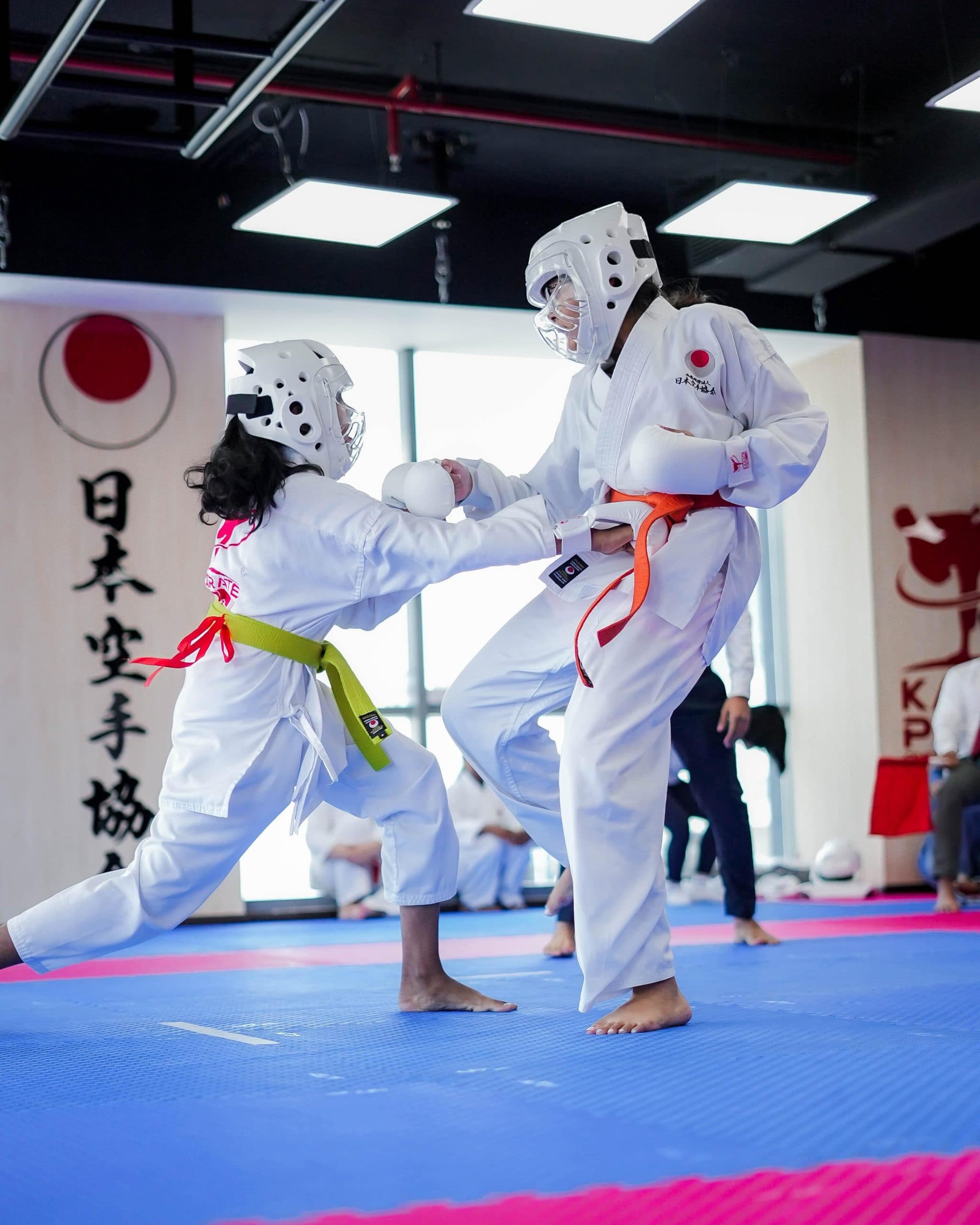 Two young students in head guards sparring on the mats beside the Karate Pro sign