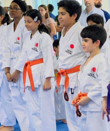 Young students in white gi and orange belts standing in line during a kids karate class