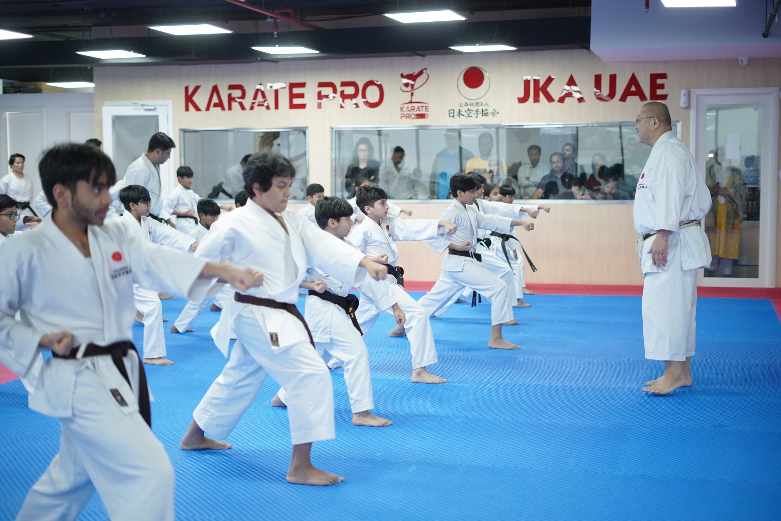 Instructor overseeing students practising a lunge punch in unison beneath the Karate Pro and JKA UAE signs