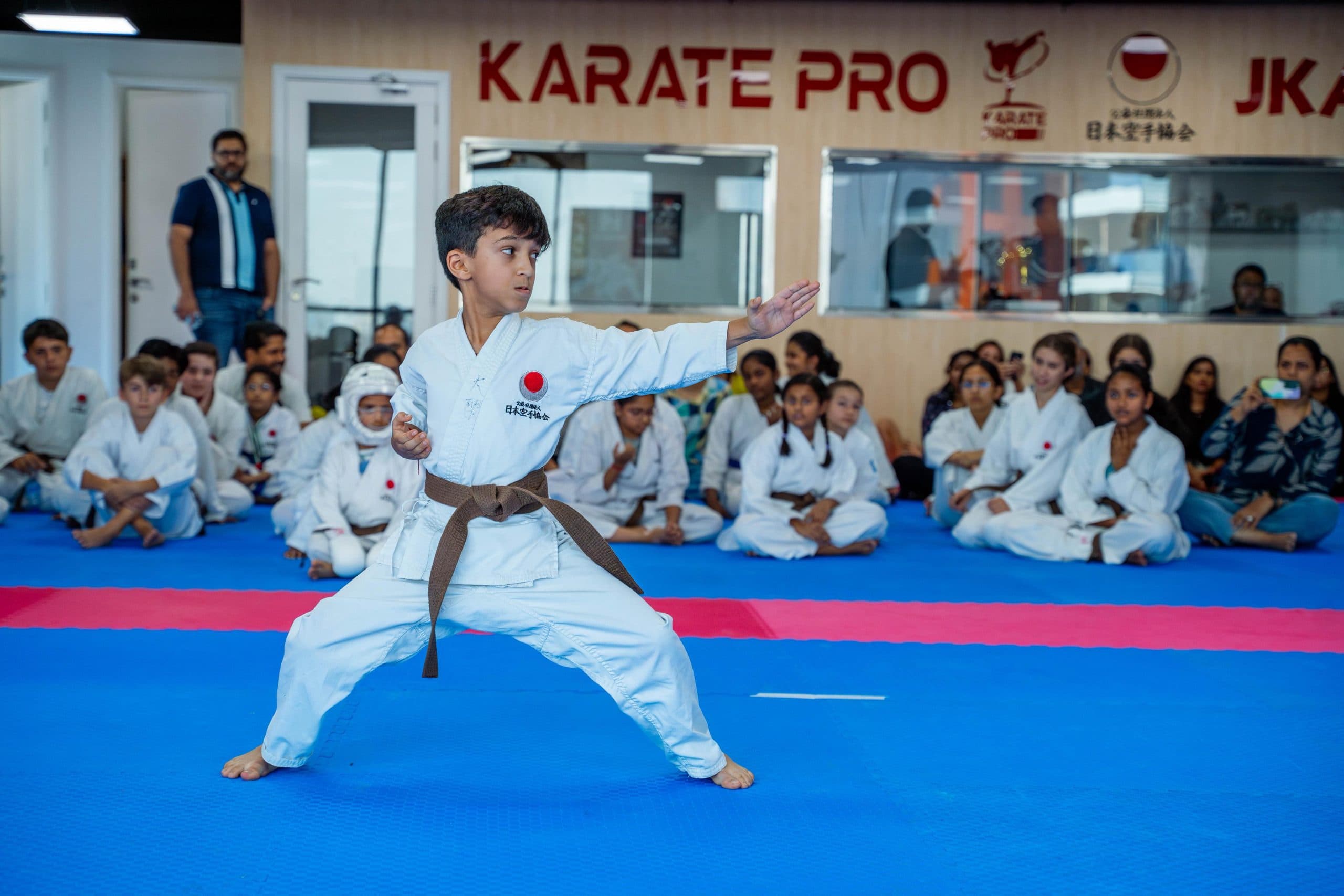 A young student performing kata in front of his seated class under the Karate Pro JKA UAE banner