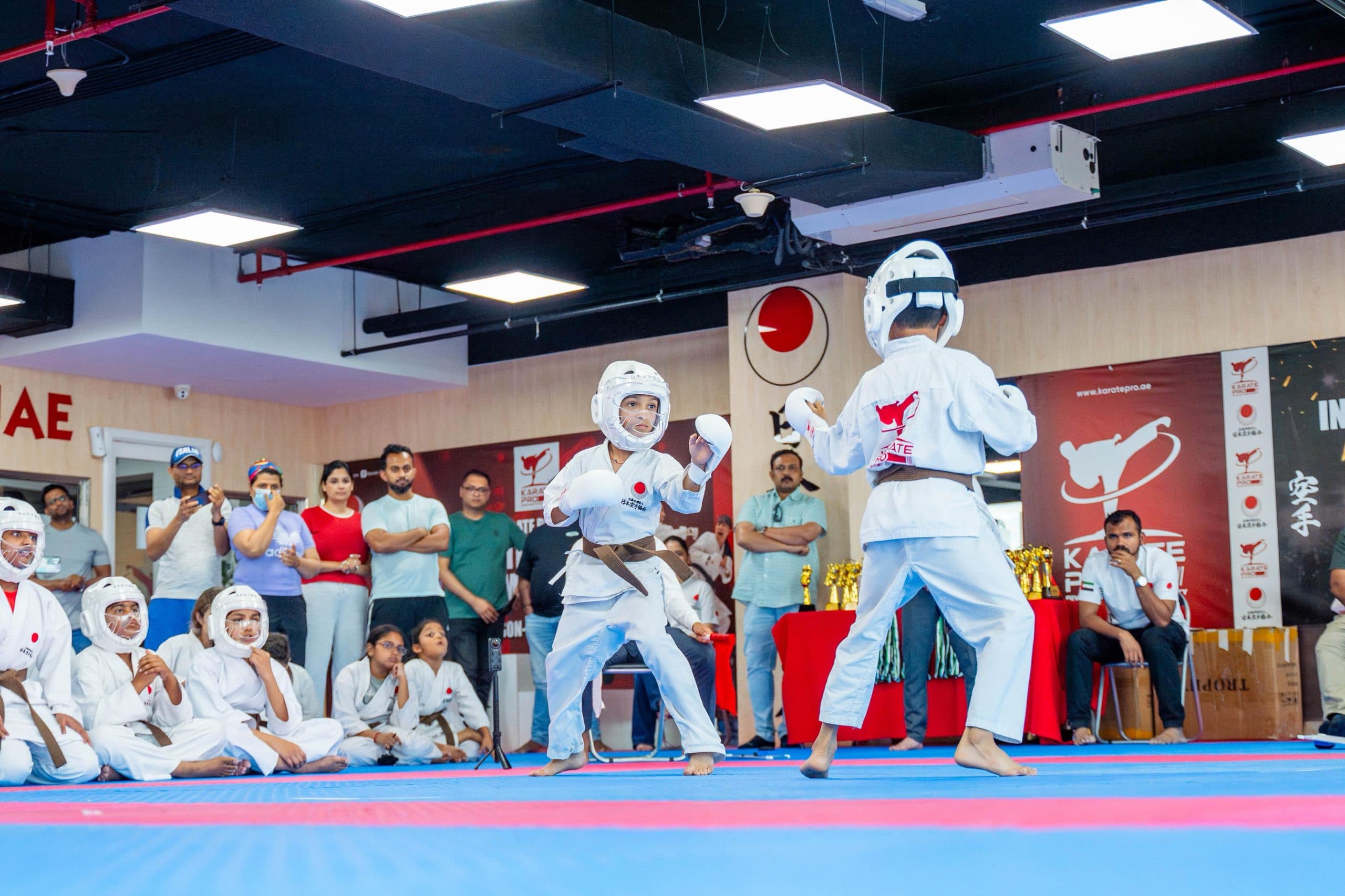 Kids sparring in headgear during a karate class while parents watch from the side
