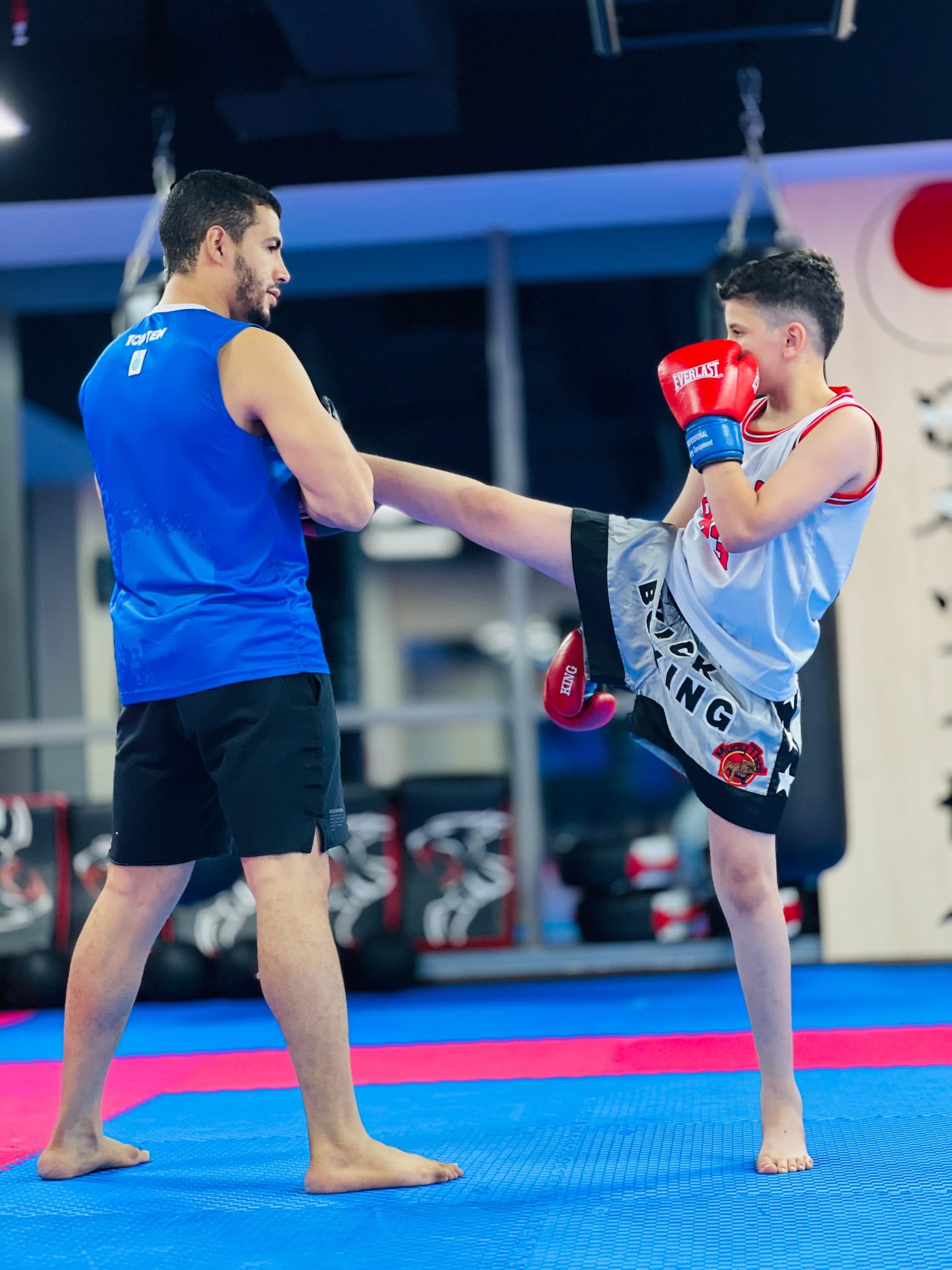 A coach holding pads for a student's kick drill at the Silicon Oasis kickboxing class