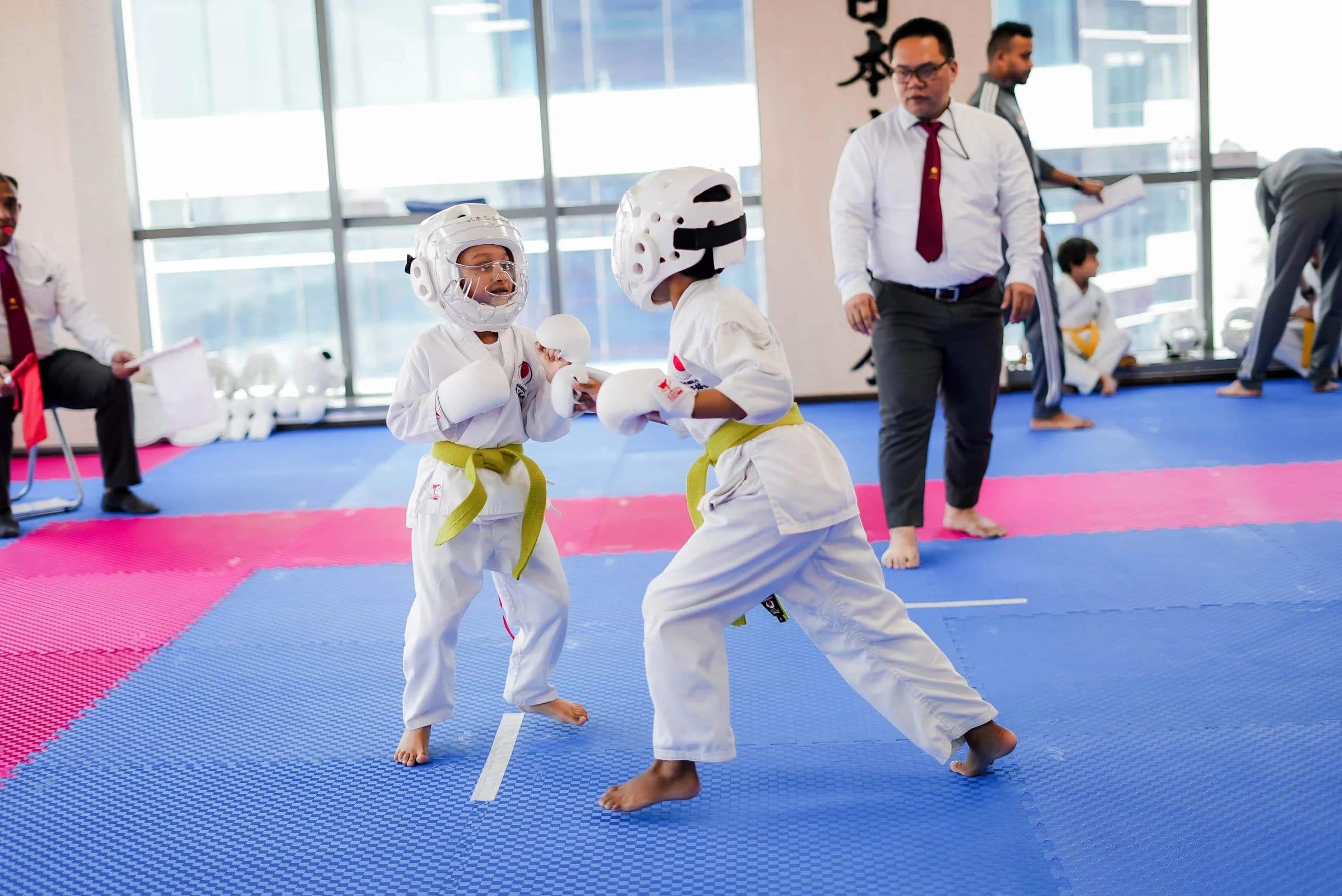 Two young students in headgear sparring at a summer karate championship as an instructor watches