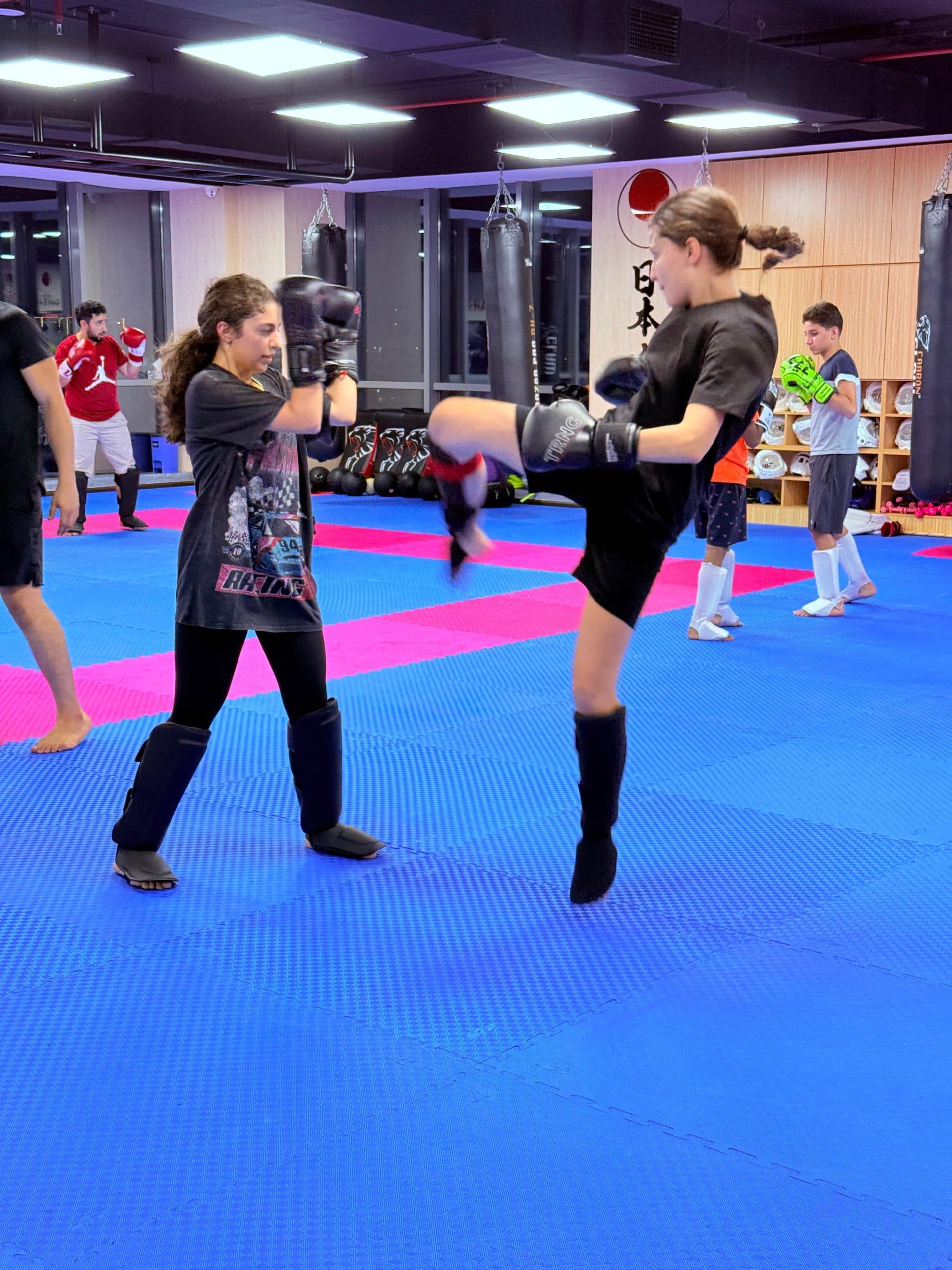 A teenager landing a kick on a heavy bag in a kickboxing class