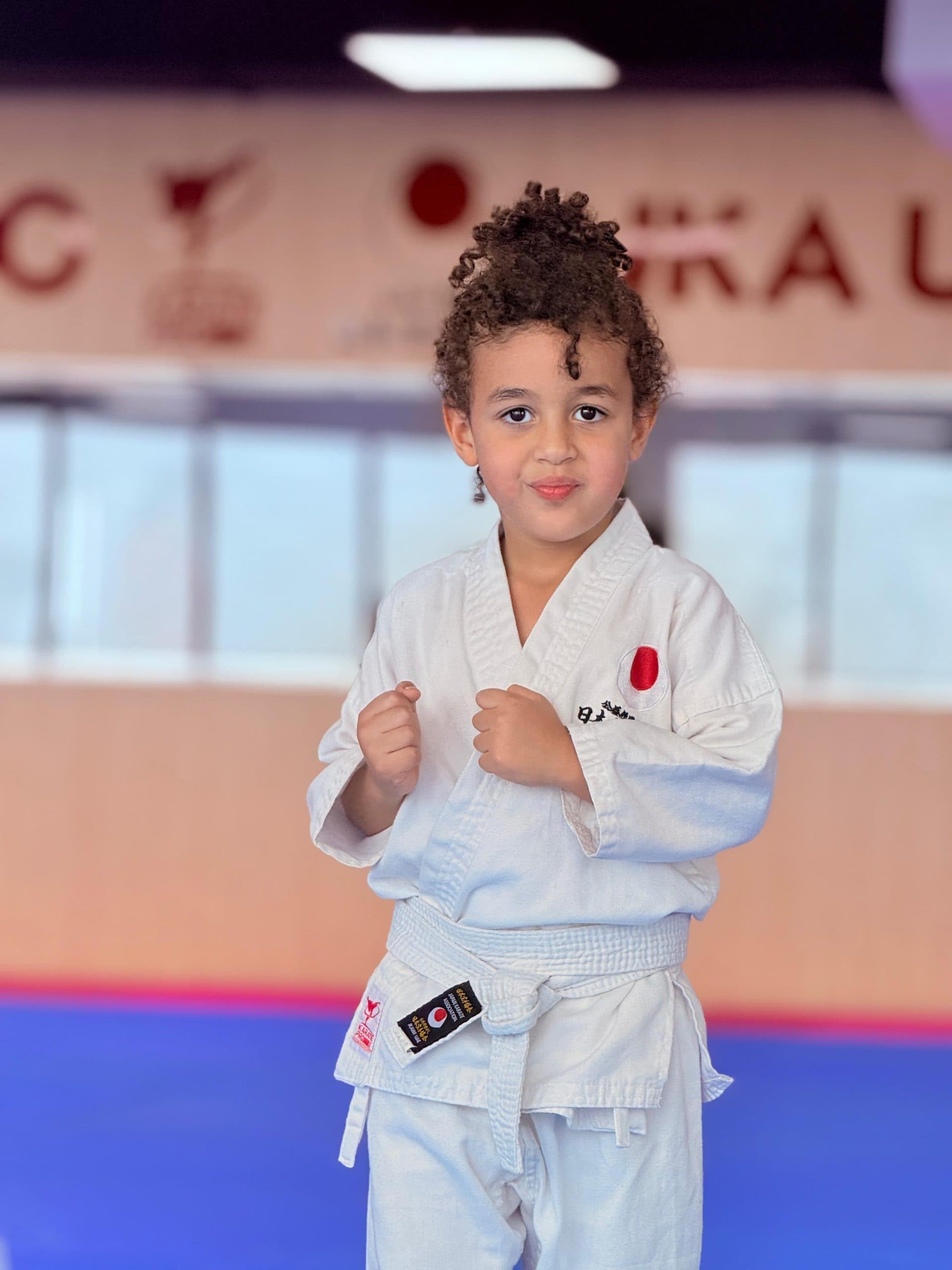 A young child in white gi proudly wearing a new karate belt