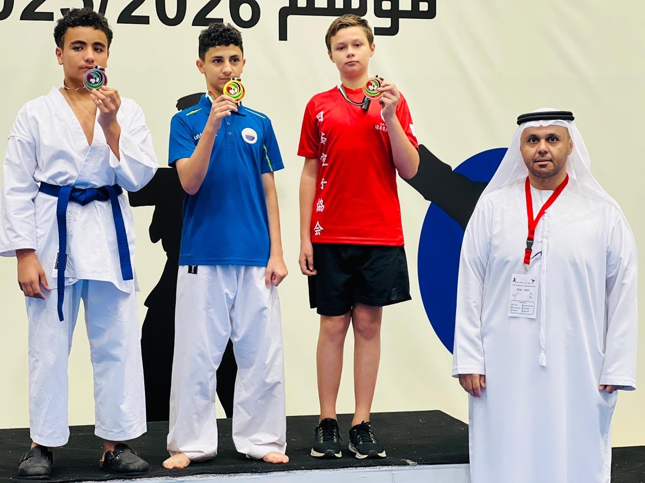 Three teenage medallists on the podium biting their medals at a karate competition