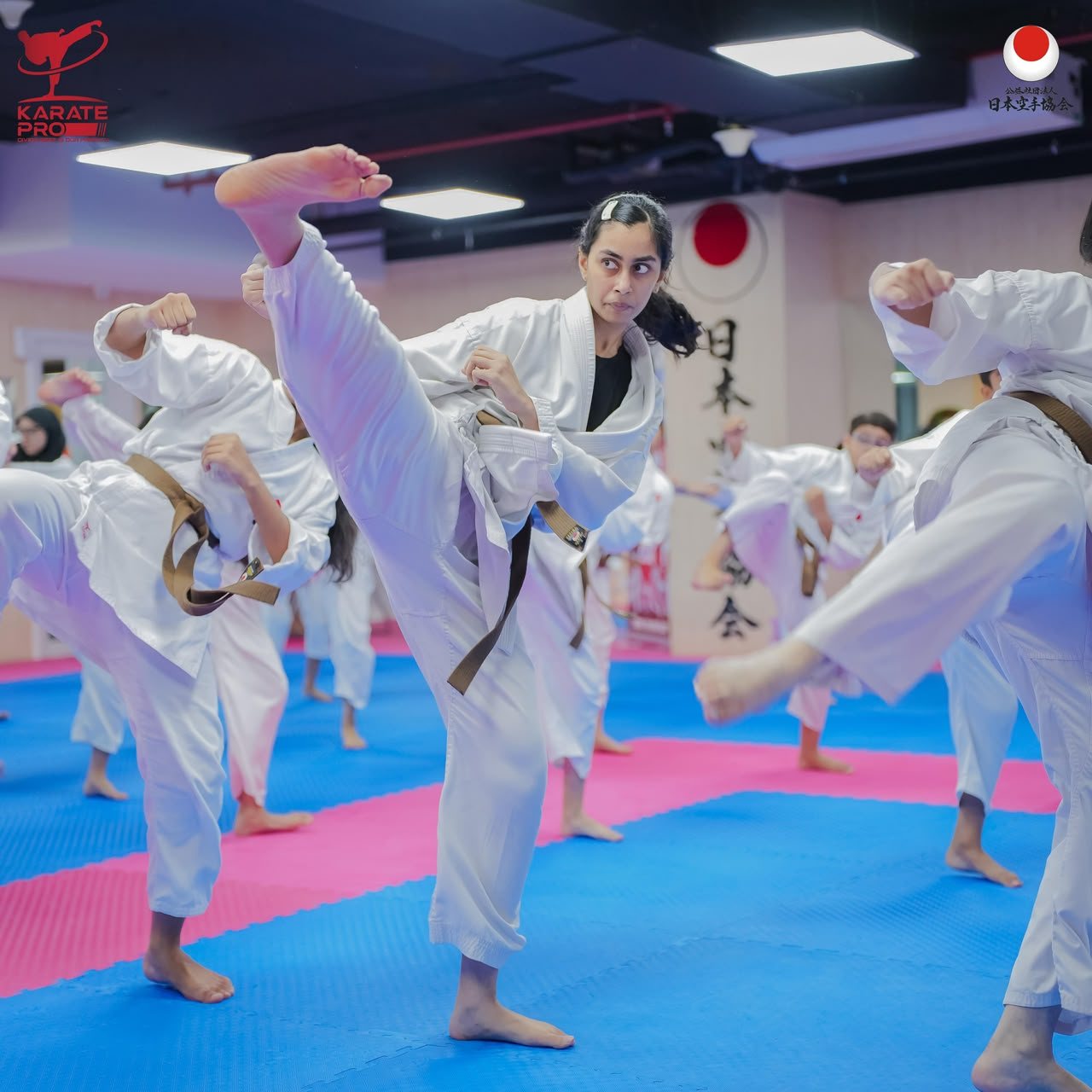 Teenage karate student throwing a high front kick in a class drill on the dojo mats